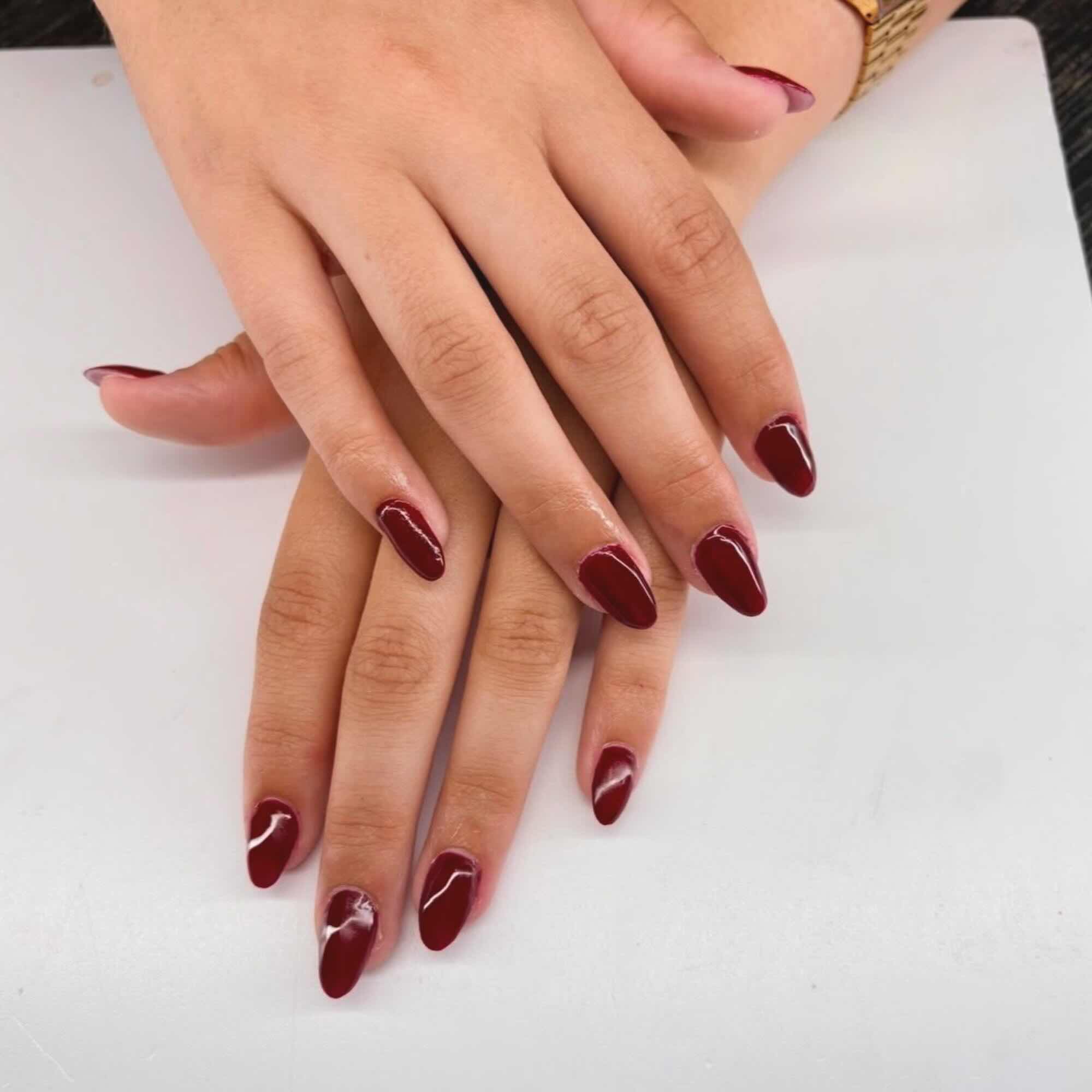 Verzorgde amandelvormige nagels in een diepe bordeauxrode gellak